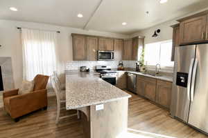 Kitchen with stainless steel appliances, a kitchen bar, a peninsula, light wood-style flooring, and light stone counters