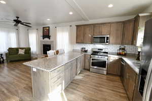 Kitchen featuring light stone countertops, stainless steel appliances, a peninsula, backsplash, and recessed lighting