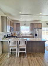 Kitchen featuring a breakfast bar area, light stone countertops, stainless steel appliances, a peninsula, and backsplash