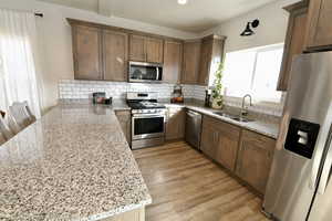 Kitchen featuring stainless steel appliances, light stone counters, wood finish cabinets, light wood-type flooring, and a peninsula