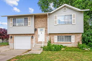 Raised ranch featuring an attached garage, a front yard, and brick siding
