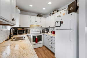 Kitchen with white appliances, backsplash, light stone countertops, white cabinets, and pendant lighting