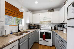 Kitchen featuring white appliances, decorative light fixtures, light stone counters, light wood finished floors, and dual tone cabinetry