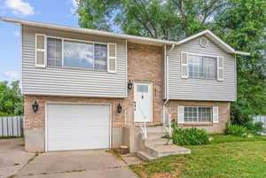 Raised ranch featuring a garage, brick siding, and driveway