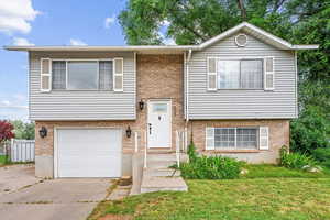 Bi-level home featuring a garage, a front yard, and brick siding