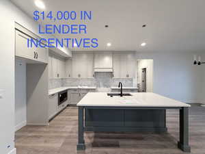 Kitchen featuring gray cabinets, recessed lighting, a breakfast bar, light wood-type flooring, and a center island with sink