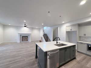 Kitchen featuring dishwasher, a center island with sink, a fireplace, open floor plan, and recessed lighting