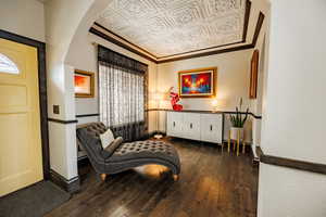 Living area with an ornate ceiling, dark wood-style flooring, arched walkways, and ornamental molding