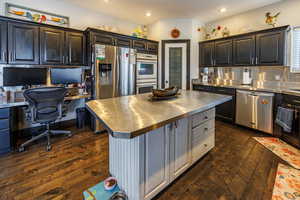 Kitchen featuring stainless steel countertops, stainless steel appliances, dark wood-style flooring, a kitchen island, and recessed lighting
