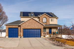 View of front of property featuring stucco siding, a garage, a porch, solar panels, and driveway