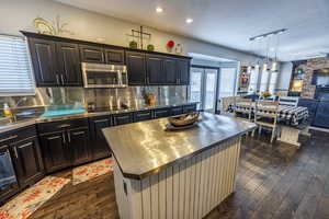 Kitchen featuring stainless steel counters, open floor plan, a center island, stainless steel microwave, and decorative backsplash