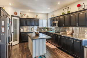 Kitchen featuring stainless steel countertops, stainless steel appliances, decorative backsplash, dark wood-style floors, and recessed lighting