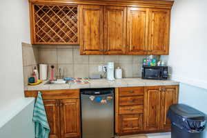 Kitchen with wood finish cabinets, stainless steel dishwasher, backsplash, black microwave, and tile counters