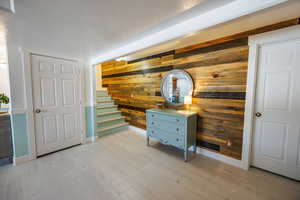 Hall with wooden walls, a textured ceiling, and light wood-type flooring