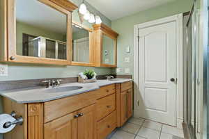 Bathroom with double vanity, light tile patterned floors, and a stall shower
