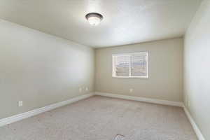Carpeted spare room featuring a textured ceiling and baseboards