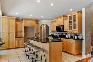 Kitchen featuring arched walkways, a kitchen bar, stainless steel appliances, a kitchen island with sink, and glass insert cabinets