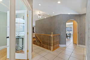 Hallway with an upstairs landing, recessed lighting, light tile patterned floors, arched walkways, and vaulted ceiling