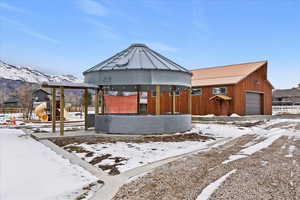 Snow covered property featuring a gazebo, a patio, a mountain view, an outbuilding, and a detached garage