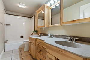 Bathroom with double vanity, light tile patterned floors, and shower / washtub combination