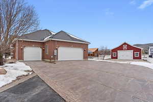 View of side of home featuring brick siding, an outbuilding, and roof with shingles