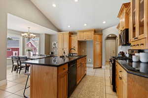 Kitchen with vaulted ceiling, black appliances, glass fronted cabinets, a kitchen bar, and suspended lighting