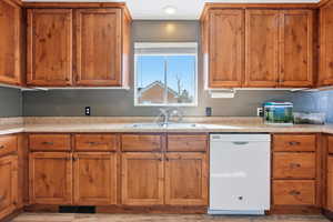 Kitchen with wood finish cabinetry, white dishwasher, and light countertops