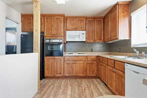 Kitchen with wood finish cabinets, white appliances, and light wood-type flooring