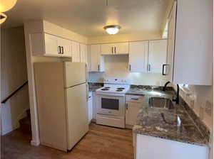 Kitchen featuring white appliances, dark stone countertops, white cabinetry, and light wood-style floors
