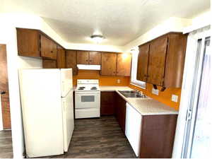 Kitchen featuring white appliances, light countertops, a textured ceiling, and dark wood-type flooring