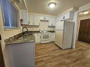 Kitchen featuring dark stone countertops, white appliances, white cabinetry, a textured ceiling, and light wood finished floors