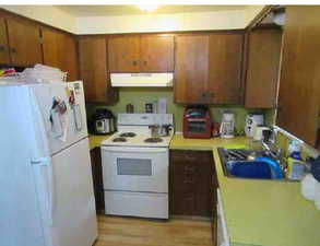 Kitchen with white appliances, light countertops, wood finish cabinets, and light wood-style floors