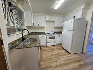 Kitchen with white appliances, a textured ceiling, white cabinetry, light wood-style flooring, and dark stone counters