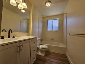 Full bathroom with vanity, dark wood-style floors, washtub / shower combination, and a textured ceiling