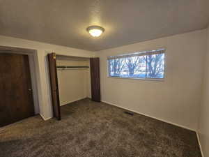 Unfurnished bedroom featuring a textured ceiling, dark colored carpet, and a closet