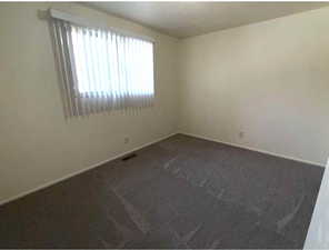 Spare room featuring dark colored carpet and baseboards