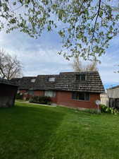 Back of house with brick siding, mansard roof, and a yard