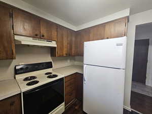 Kitchen featuring electric range oven, freestanding refrigerator, light countertops, dark wood-type flooring, and dark wood finish cabinetry