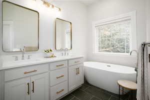 Bathroom featuring a freestanding bath, double vanity, and dark tile patterned floors