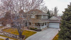 View of front of property featuring covered porch, driveway, a shingled roof, a front lawn, and a garage