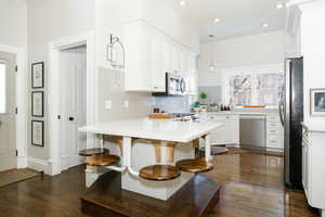 Kitchen with a peninsula, stainless steel appliances, white cabinets, dark wood-style flooring, and a breakfast bar area