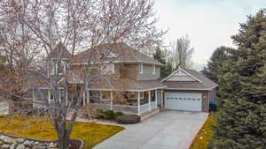 View of front facade with a porch, driveway, roof with shingles, and a front lawn