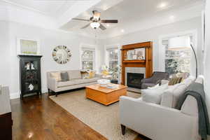 Living room with wood finished floors, a tiled fireplace, a ceiling fan, crown molding, and recessed lighting