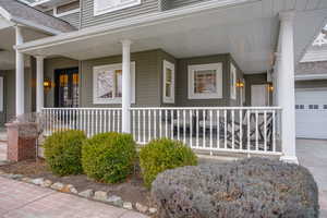 View of exterior entry with a porch, a shingled roof, and concrete driveway