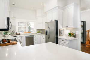 Kitchen with stainless steel appliances, white cabinets, hanging light fixtures, and decorative backsplash