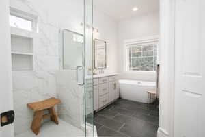 Bathroom featuring vanity, a marble finish shower, a freestanding tub, and dark tile patterned flooring