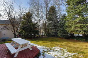 Snowy yard featuring a lawn, outdoor dining area, and a deck