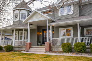 Property entrance featuring covered porch, a shingled roof, and a yard