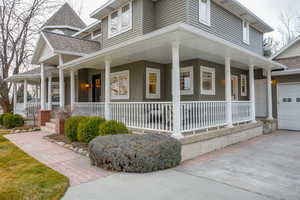 View of side of home with a large porch, a shingled roof, driveway, and a garage