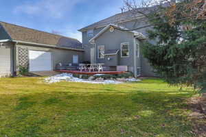 Back of house with a lawn, a garage, a deck, and a shingled roof